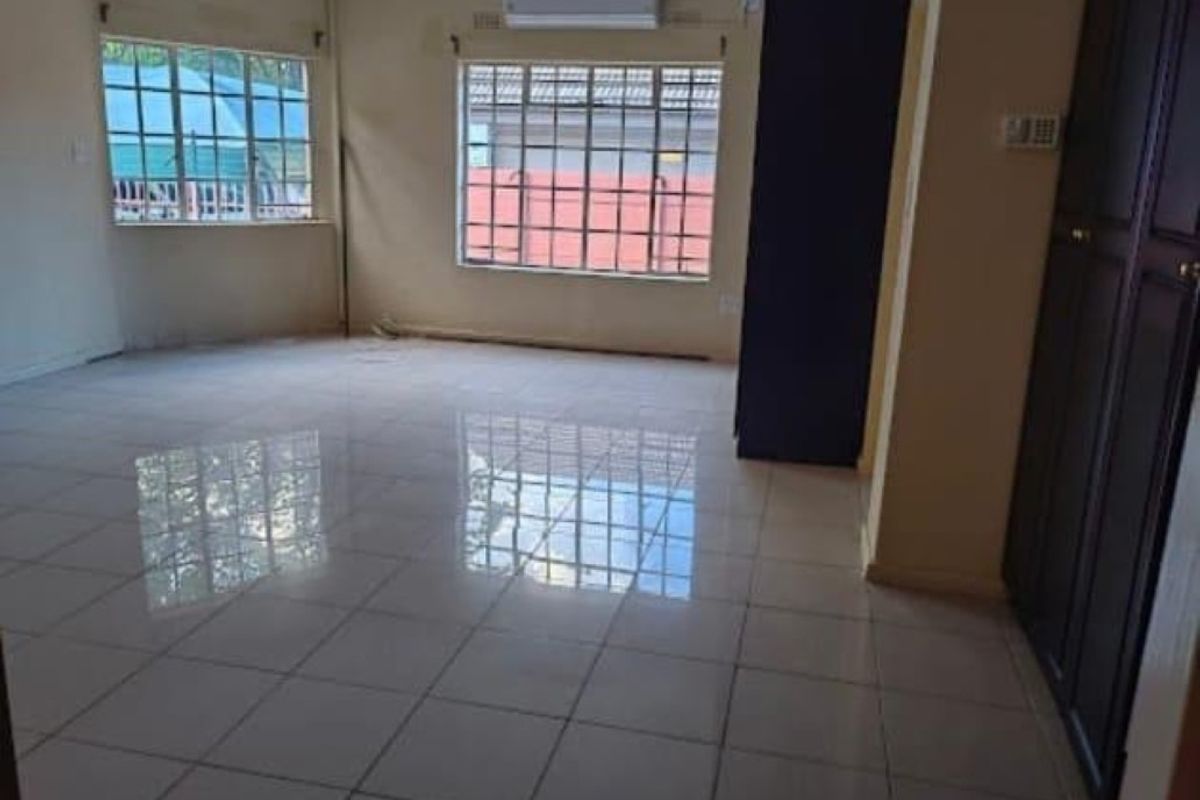 Spacious, empty living area featuring polished tiled flooring, a wall-mounted air conditioning unit, and built-in storage cupboards.