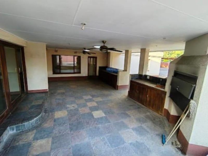 Spacious covered patio featuring a built-in braai, tiled flooring, and built-in cabinetry, offering a functional outdoor entertainment area.