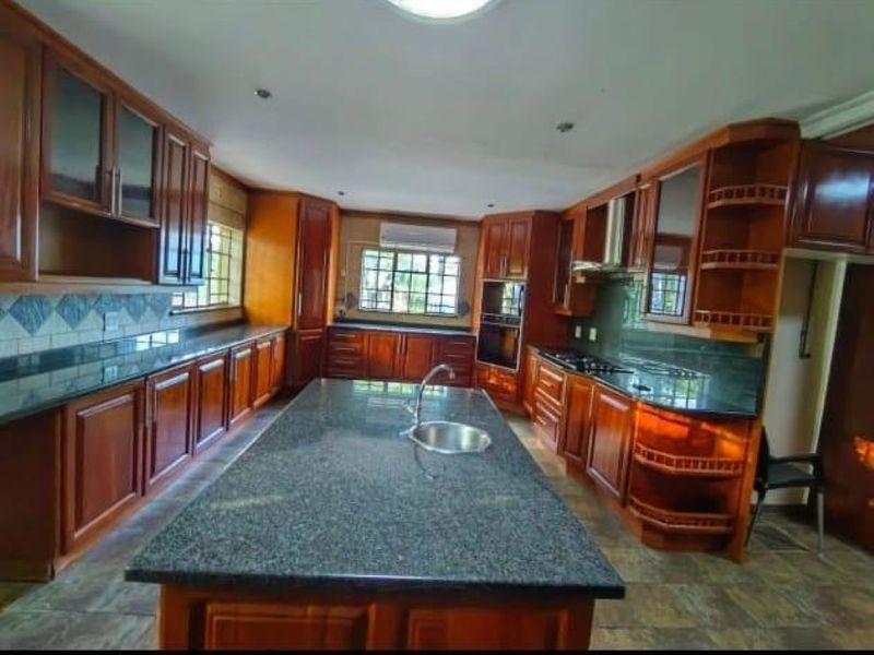 Spacious kitchen featuring extensive wooden cabinetry, granite countertops, a central island with a prep sink, and built-in appliances.