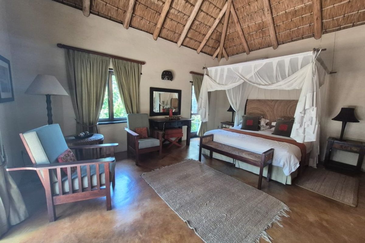Spacious bedroom featuring a high vaulted thatched roof with exposed timber rafters and polished concrete flooring, creating a rustic and airy atmosphere.