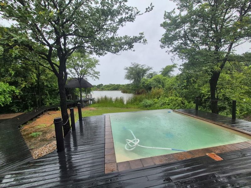 Outdoor pool area featuring timber decking, a thatched gazebo, and direct views of the surrounding natural landscape and water.