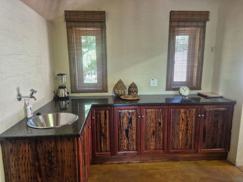 A kitchen area featuring custom timber cabinetry, dark granite countertops, an undermount stainless steel sink, and bamboo window blinds.