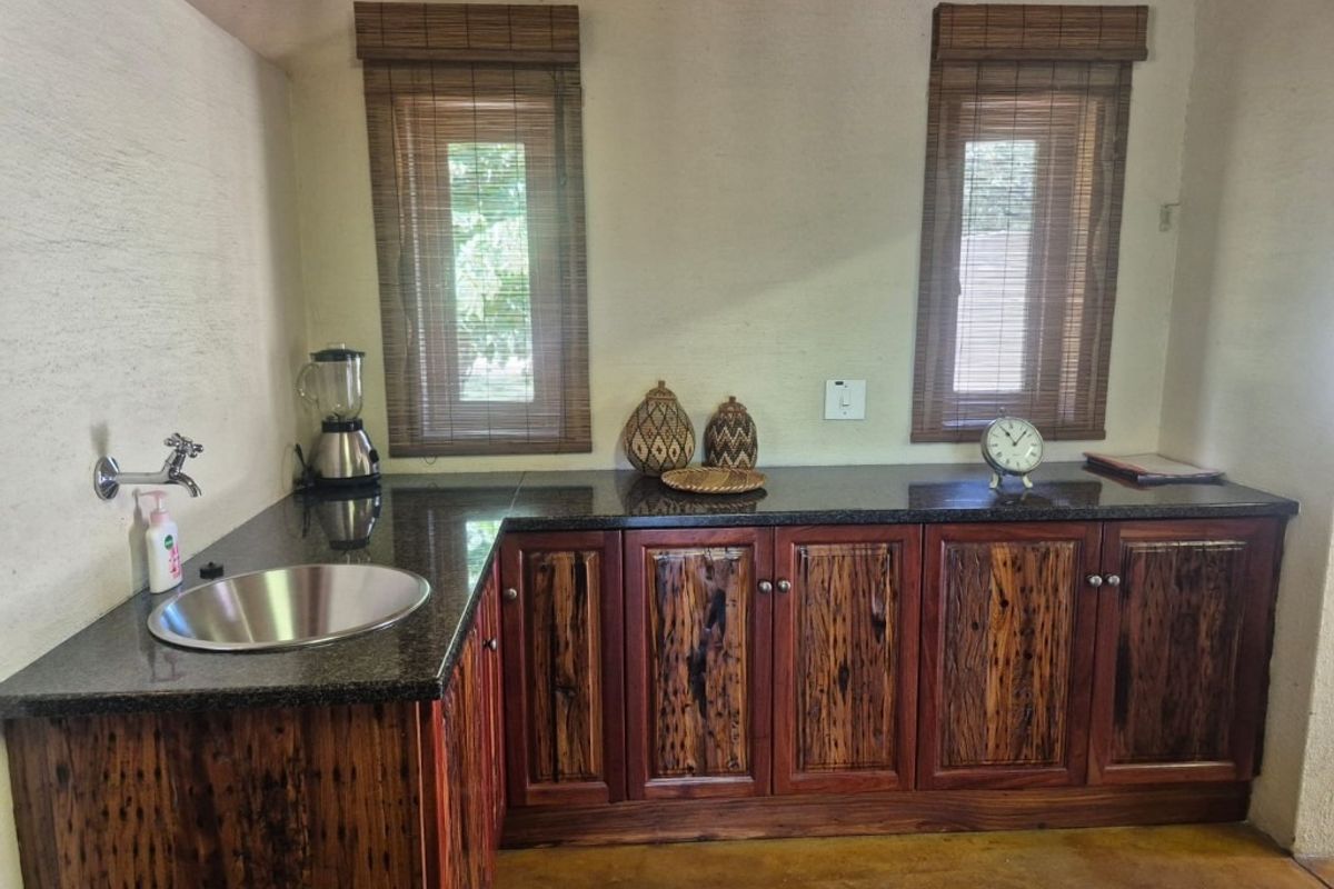 A kitchen area featuring custom timber cabinetry, dark granite countertops, an undermount stainless steel sink, and bamboo window blinds.