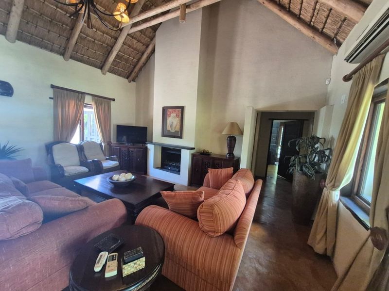 Spacious living room featuring a high vaulted thatched ceiling with exposed timber trusses, a central built-in fireplace, and tiled flooring.