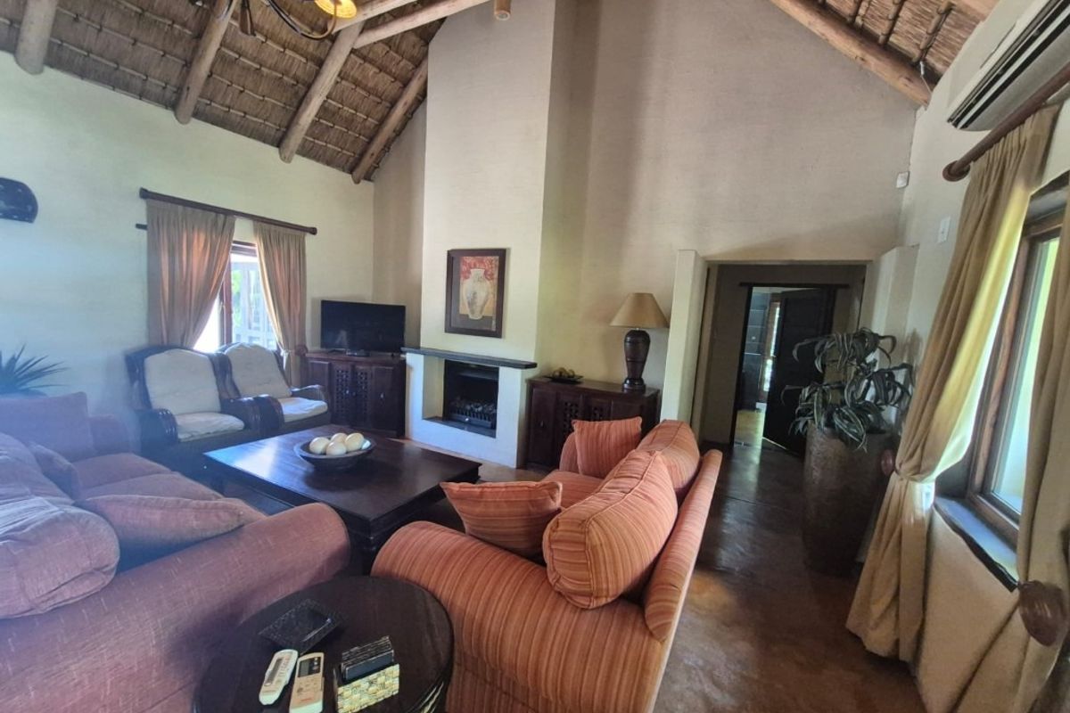 Spacious living room featuring a high vaulted thatched ceiling with exposed timber trusses, a central built-in fireplace, and tiled flooring.