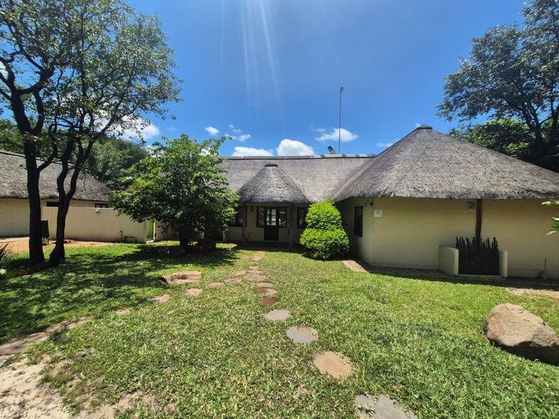 A well-maintained rear exterior view of a house featuring a traditional thatch roof, a stone pathway, and a spacious garden area.