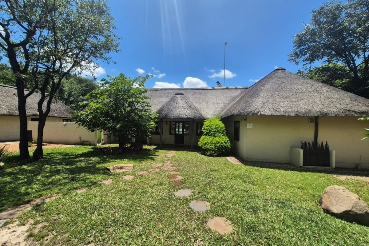 A well-maintained rear exterior view of a house featuring a traditional thatch roof, a stone pathway, and a spacious garden area.