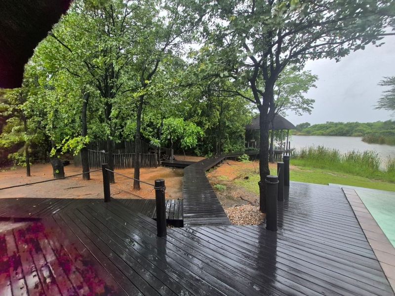 Outdoor pool area featuring extensive timber decking, a wooden walkway leading to a thatched gazebo, and scenic views of the surrounding natural landscape.