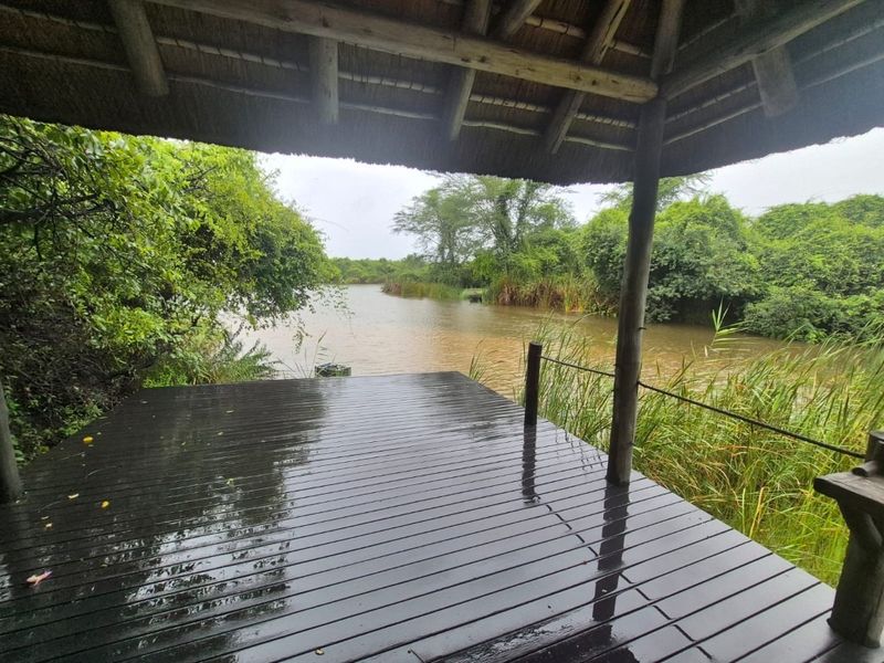 A covered outdoor timber deck with a thatched roof, offering direct views over a natural river or dam setting.