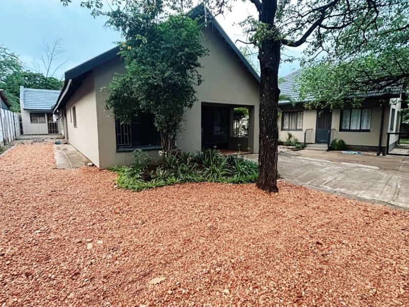 Front view of the property featuring a gravel garden, concrete driveway, and established trees with a tiled roof structure.