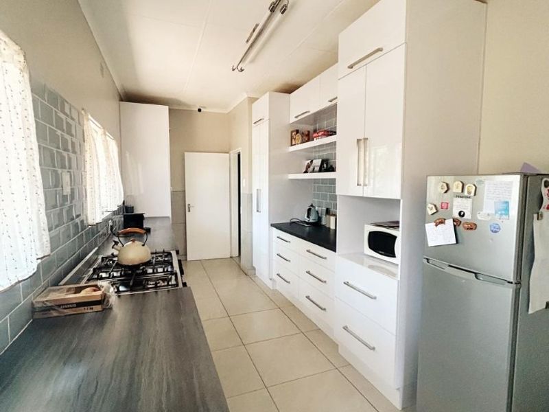 A functional galley-style kitchen featuring white cabinetry, dark laminate countertops, a gas hob, and a subway tile backsplash with neutral floor tiling.