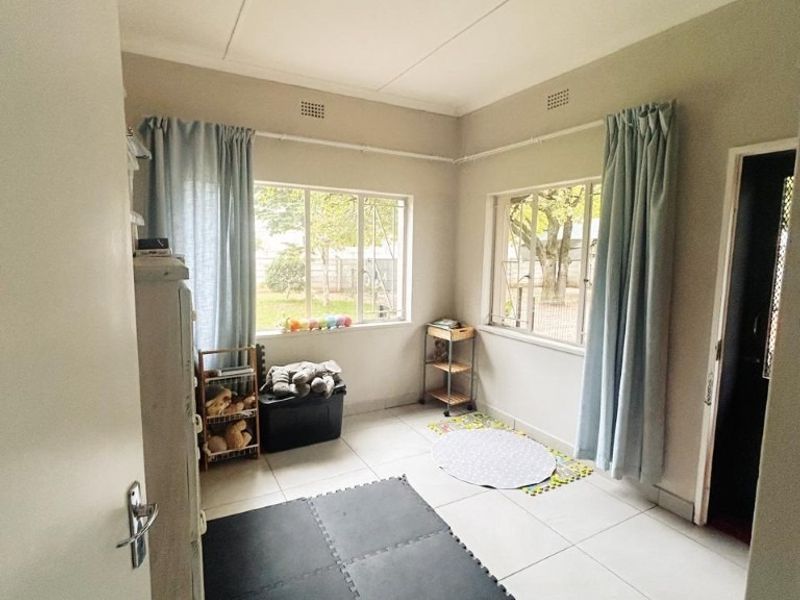 A bright, neutral bedroom featuring large windows, tiled flooring, and a simple ceiling light fixture, offering a clean canvas for personalization.