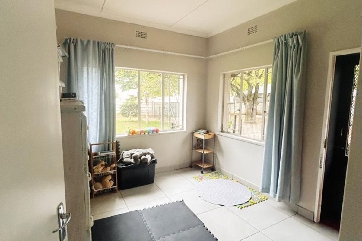 A bright, neutral bedroom featuring large windows, tiled flooring, and a simple ceiling light fixture, offering a clean canvas for personalization.