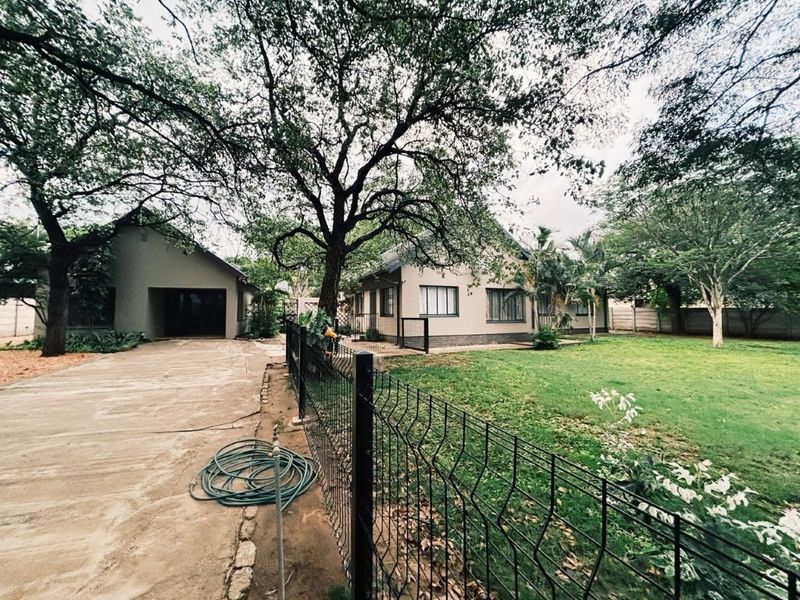 Front view of the property featuring a concrete driveway, detached garage, and a spacious garden with mature trees and perimeter fencing.