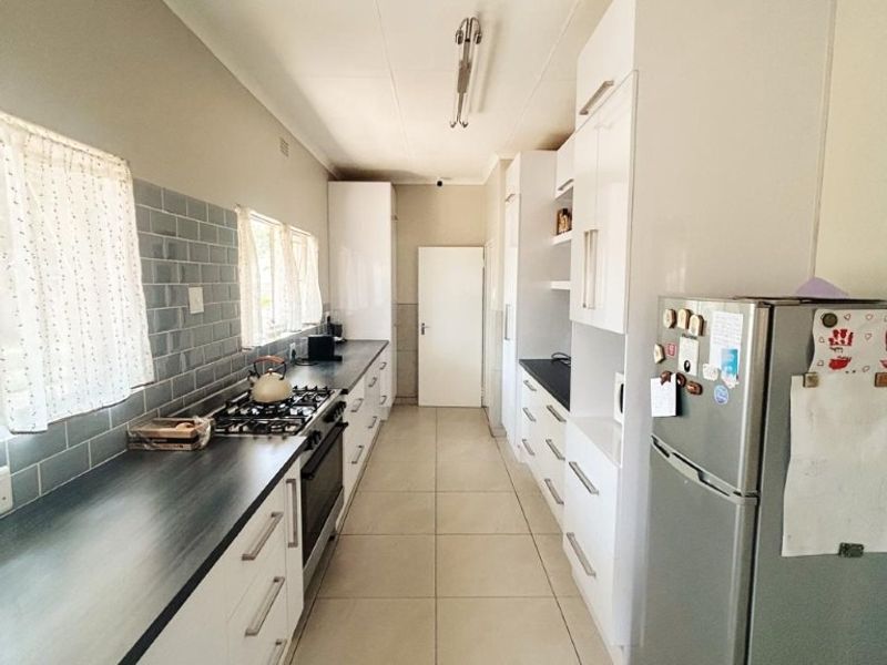 A galley-style kitchen featuring white cabinetry, dark laminate countertops, a gas hob, and modern tiled flooring with a subway tile backsplash.