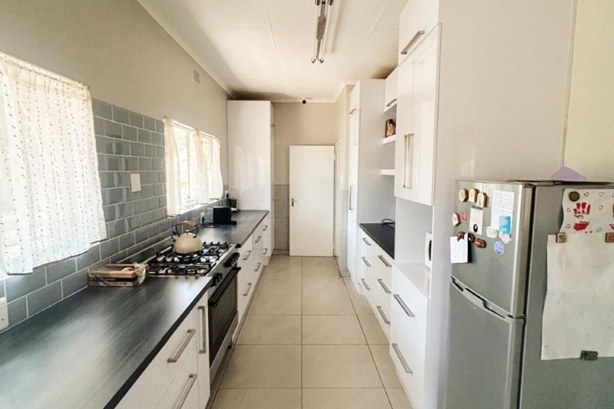 A galley-style kitchen featuring white cabinetry, dark laminate countertops, a gas hob, and modern tiled flooring with a subway tile backsplash.