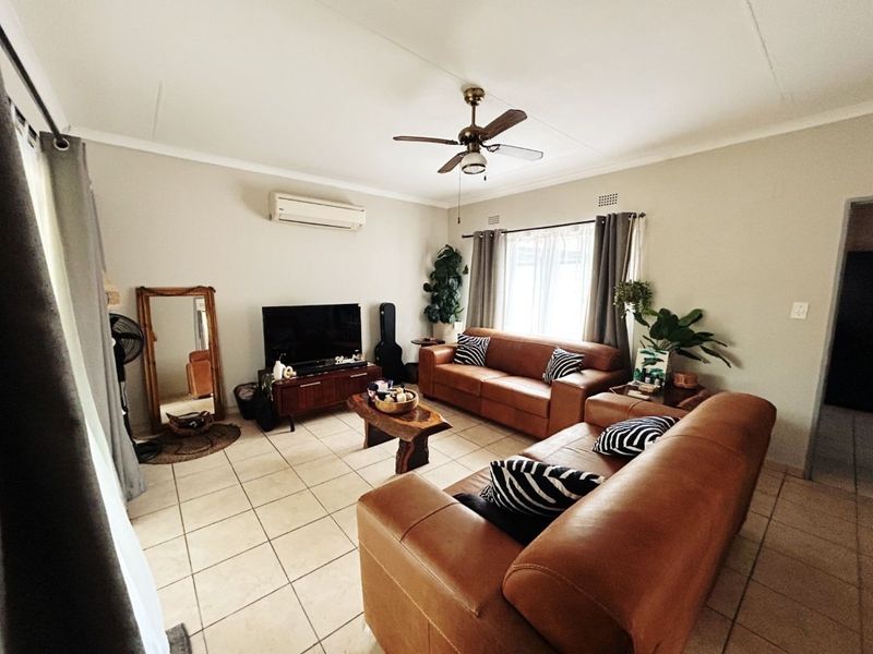 A comfortable living room featuring tiled flooring, a ceiling fan, and a wall-mounted air conditioning unit.