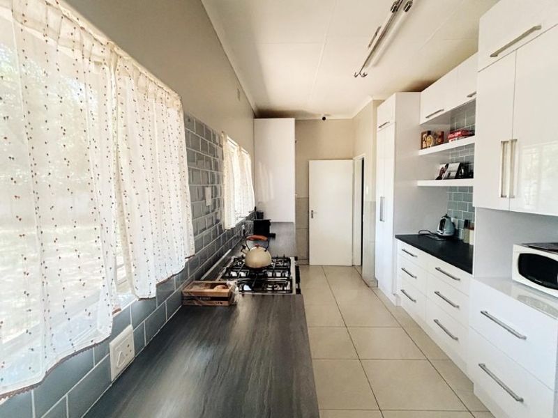 A functional galley-style kitchen featuring white cabinetry, dark laminate countertops, a gas hob, and a grey subway tile backsplash with neutral floor tiling.