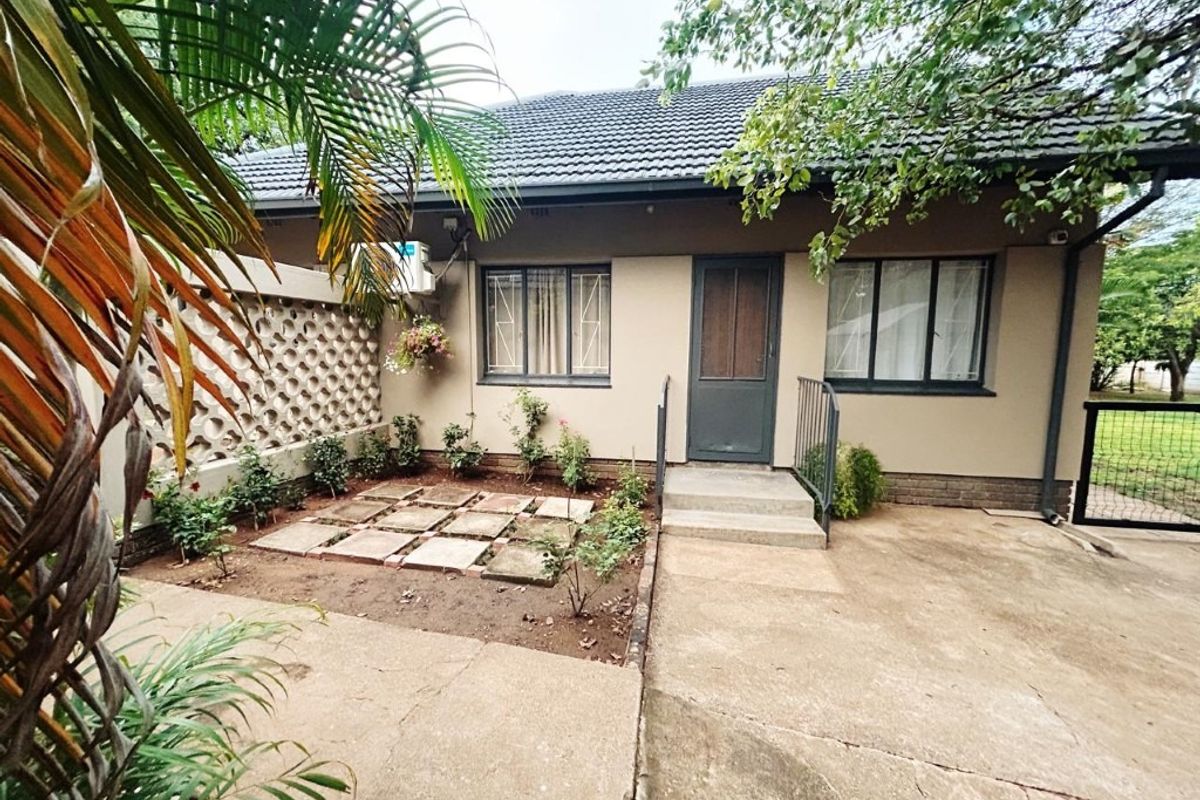Rear exterior view of the house featuring a concrete patio area, breeze block boundary wall, and established garden beds.
