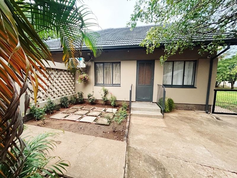 Rear exterior view of the house featuring a concrete patio area, breeze block boundary wall, and established garden beds.
