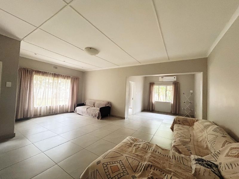 Spacious open-plan living area featuring neutral tiled flooring, large windows with natural light, and a wall-mounted air conditioning unit.