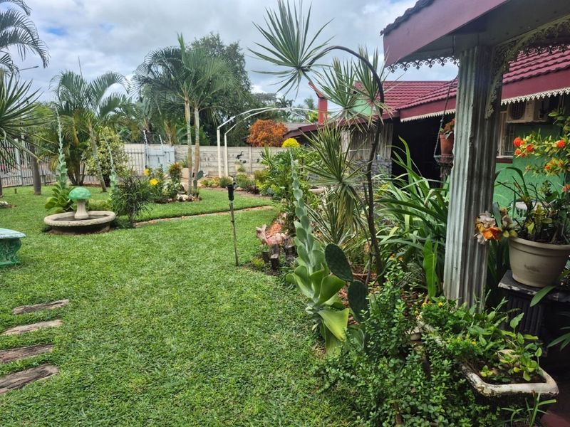 A well-maintained residential garden featuring a lush lawn, mature landscaping, and a covered patio area with decorative architectural columns.