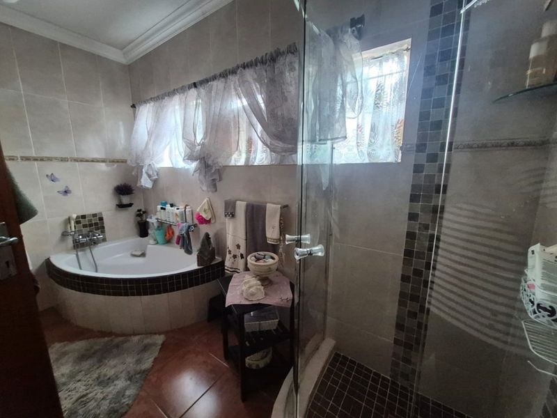 A bathroom featuring a corner bathtub, a separate glass-enclosed shower, and neutral wall tiling with decorative mosaic accents.