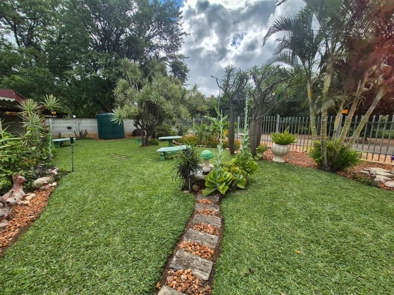 A well-maintained residential garden featuring a stone pathway, established trees, and secure perimeter fencing with a water tank.