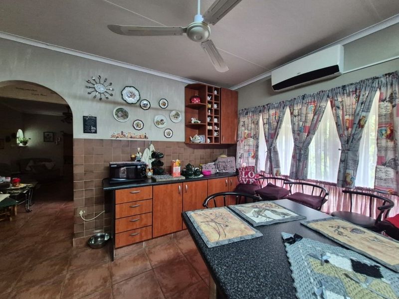 A functional kitchen area featuring built-in wooden cabinetry, tiled backsplash, and tiled flooring, equipped with a ceiling fan and wall-mounted air conditioning unit.