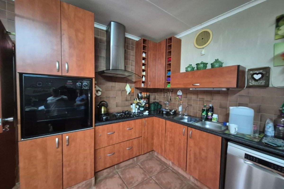A functional kitchen featuring wood-finish cabinetry, a built-in oven, gas hob, extractor fan, and tiled backsplash with durable floor tiles.