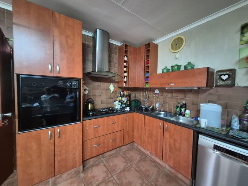 A functional kitchen featuring wood-finish cabinetry, a built-in oven, gas hob, extractor fan, and tiled backsplash with durable floor tiles.