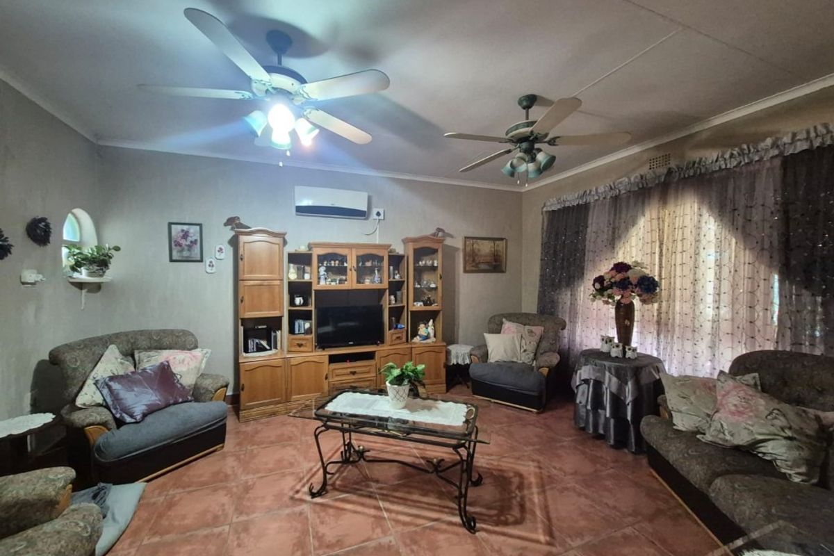 A spacious living room featuring tiled flooring, dual ceiling fans, and a wall-mounted air conditioning unit.