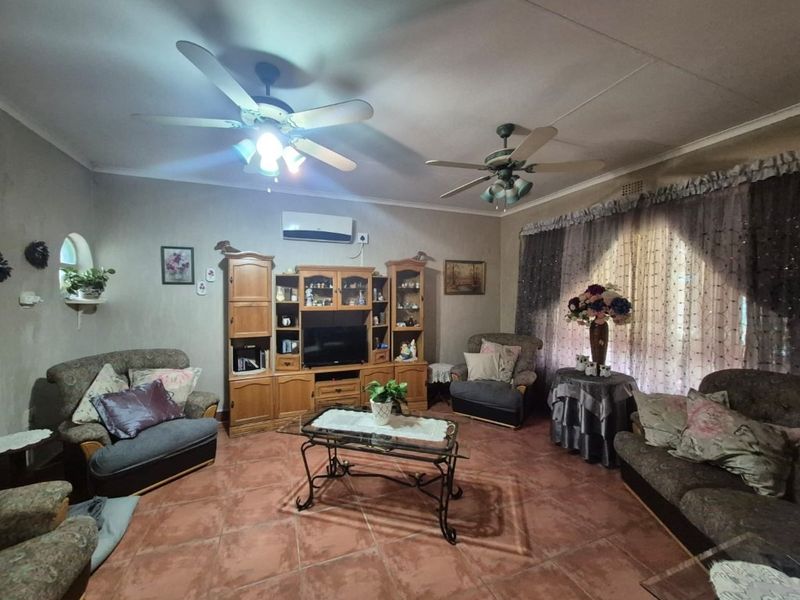 A spacious living room featuring tiled flooring, dual ceiling fans, and a wall-mounted air conditioning unit.