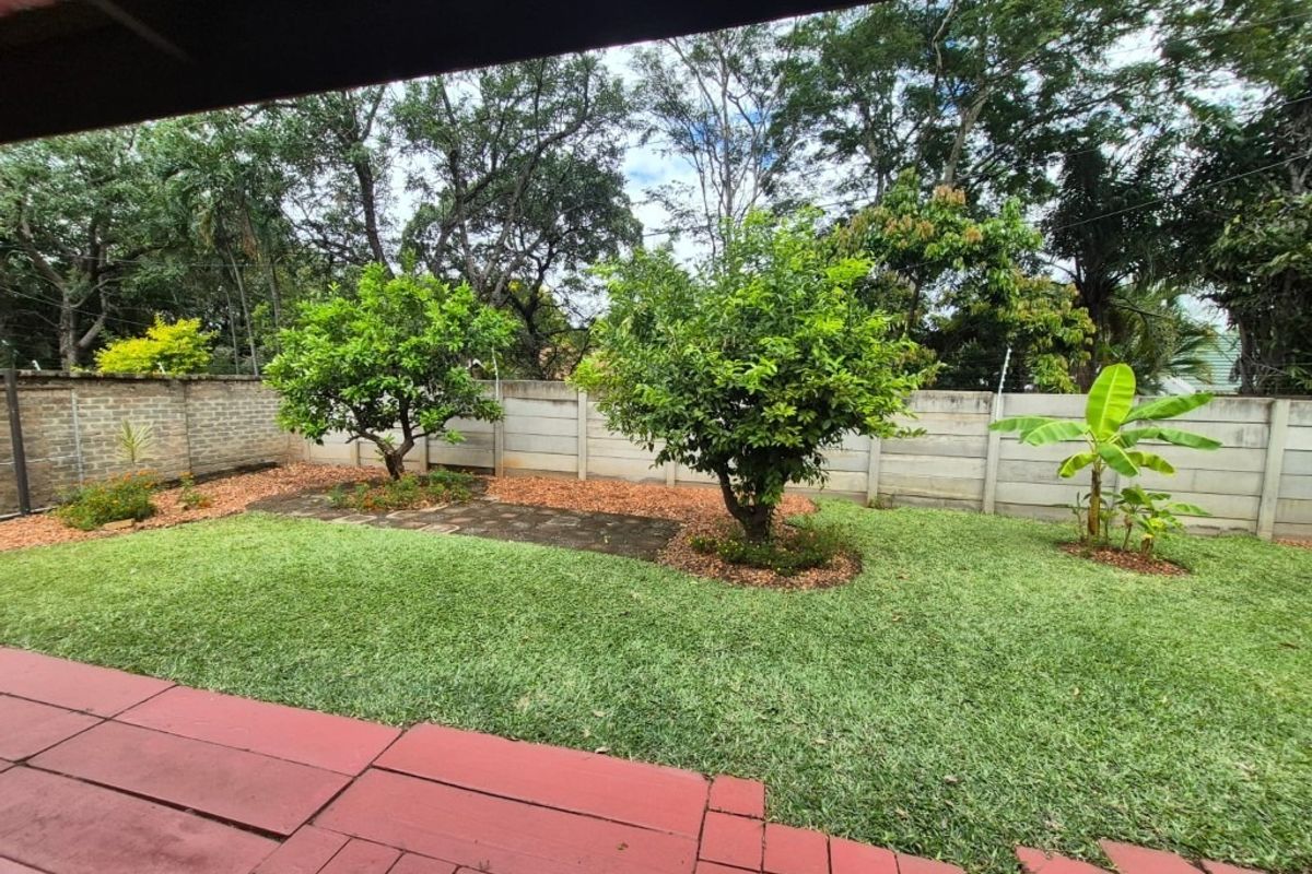 A private rear garden featuring a paved patio area, established trees, and a secure precast concrete boundary wall.