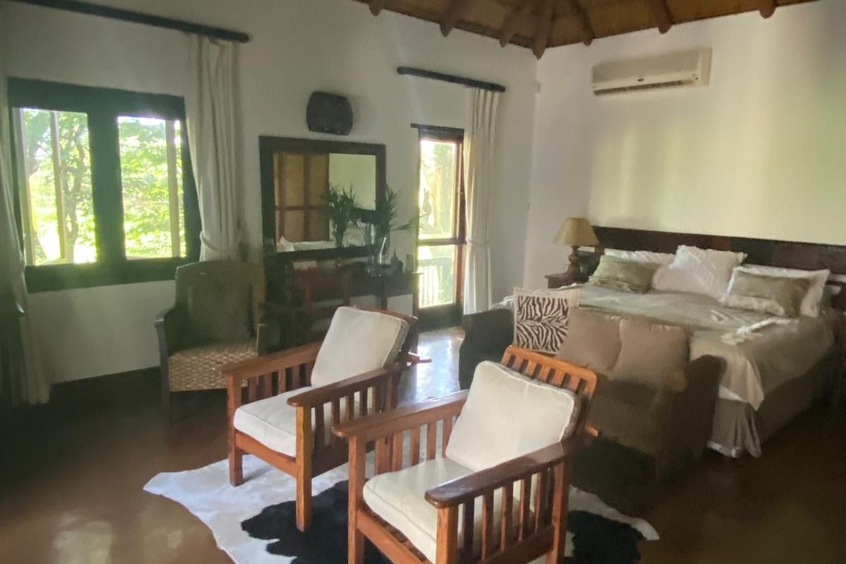 Spacious bedroom featuring a high thatched ceiling with exposed timber rafters, concrete flooring, and a wall-mounted air conditioning unit.