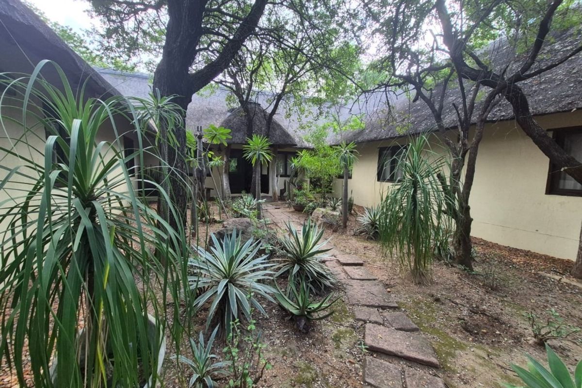 A view of the rear exterior featuring a traditional thatch roof, plastered walls, and a stone pathway winding through a landscaped garden area.