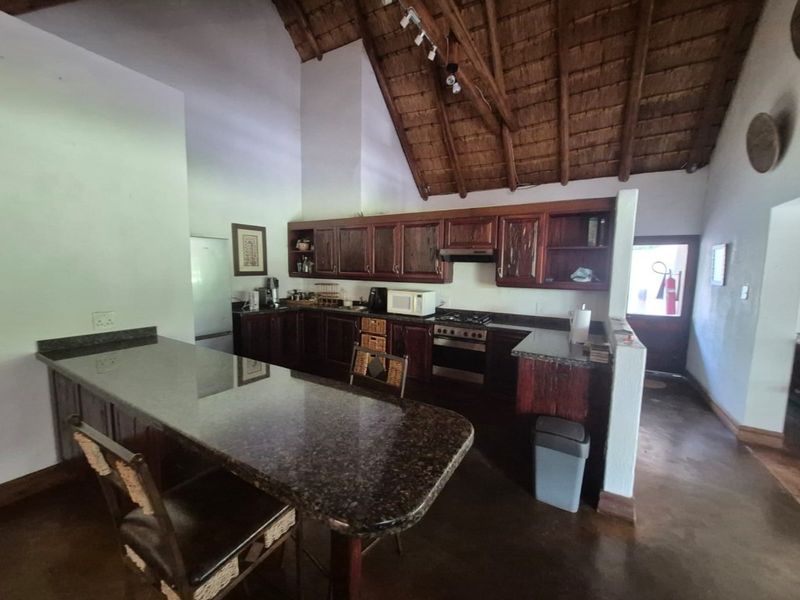Spacious kitchen featuring dark granite countertops, wooden cabinetry, built-in oven and hob, and a high exposed thatch ceiling with a breakfast bar.