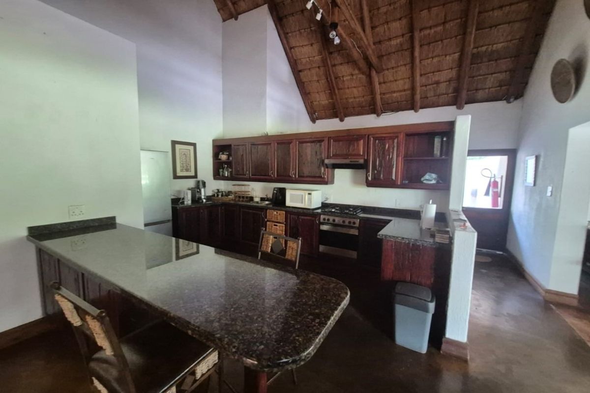 Spacious kitchen featuring dark granite countertops, wooden cabinetry, built-in oven and hob, and a high exposed thatch ceiling with a breakfast bar.