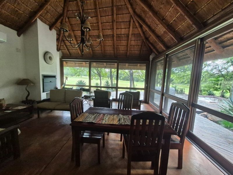 Spacious open-plan living and dining area featuring a high thatched ceiling with exposed rafters, a built-in fireplace, and expansive glass doors overlooking the garden.