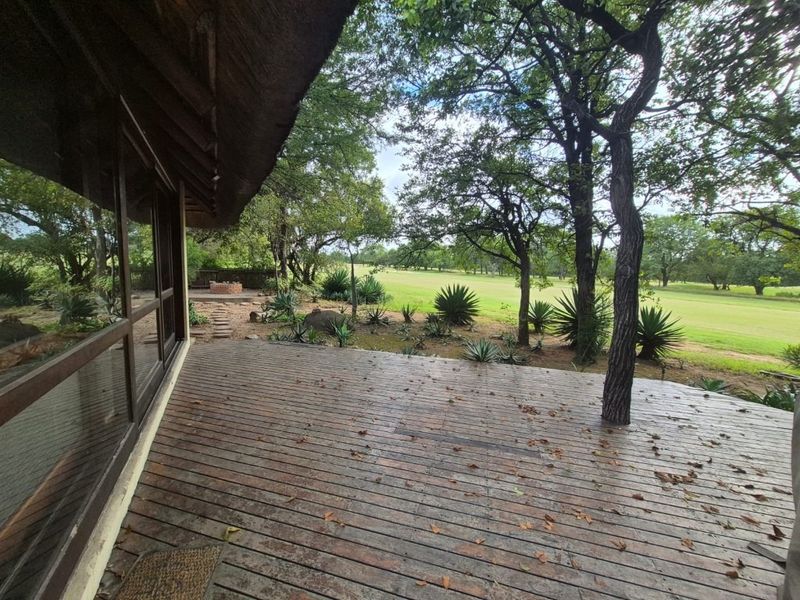 Spacious outdoor timber deck featuring a thatched roof overhang, large glass sliding doors, and a built-in fire pit overlooking the garden and golf course.