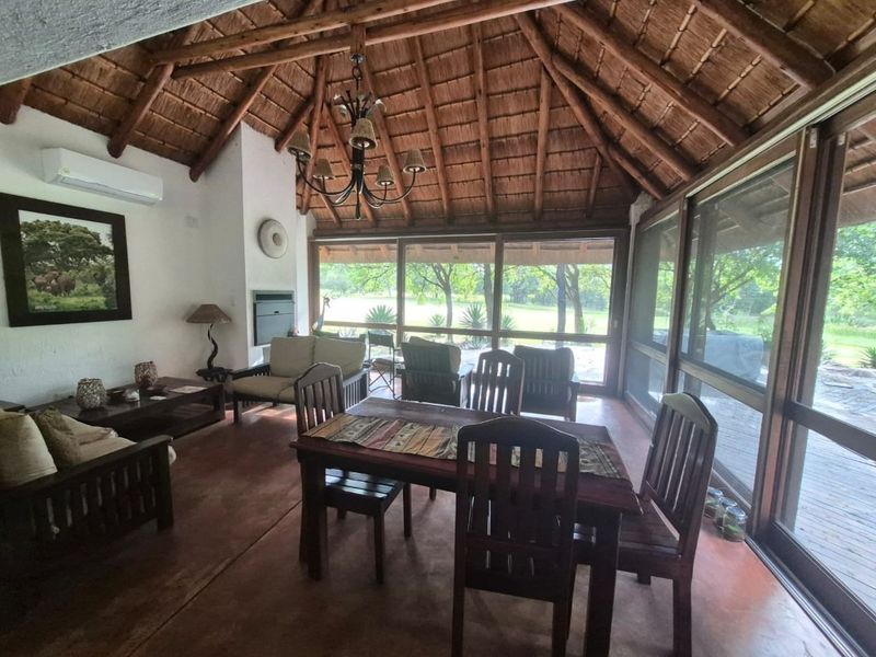 Spacious open-plan living and dining area featuring a high thatched roof with exposed timber rafters, a built-in fireplace, and large glass doors to the garden.