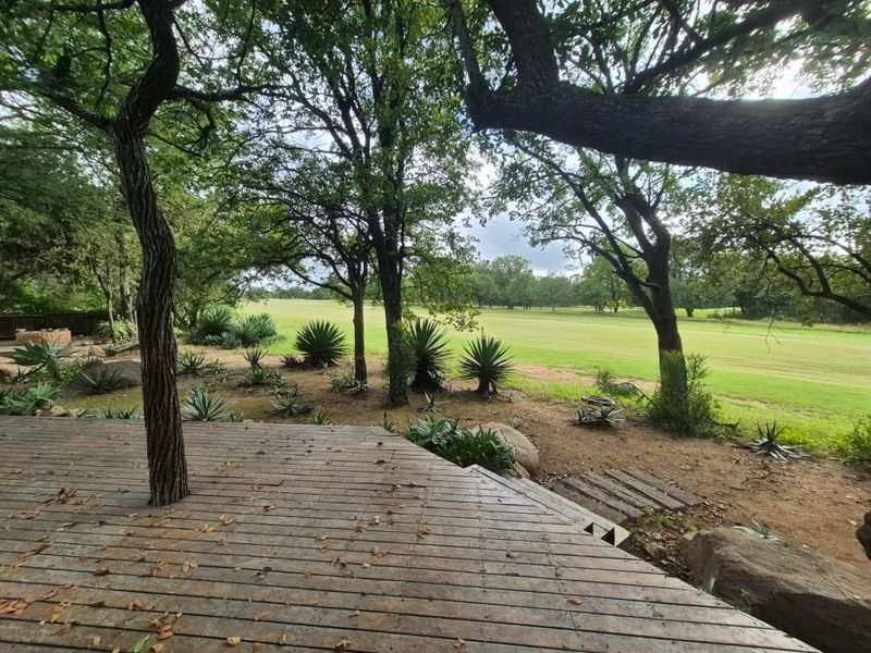 A wooden deck overlooking a spacious, tree-lined garden area with a natural landscape.
