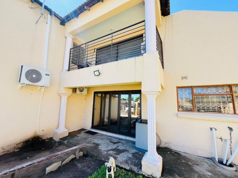 Rear exterior view of the property featuring a covered patio, upper balcony with metal railing, and sliding glass doors.