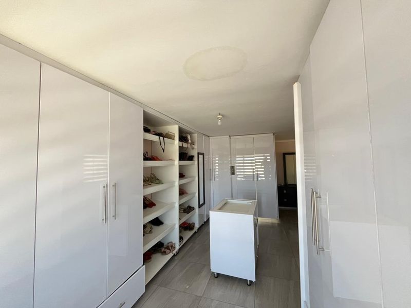 A spacious walk-in closet featuring extensive built-in cabinetry, a central island unit, and tiled flooring, showing a visible water stain on the ceiling.