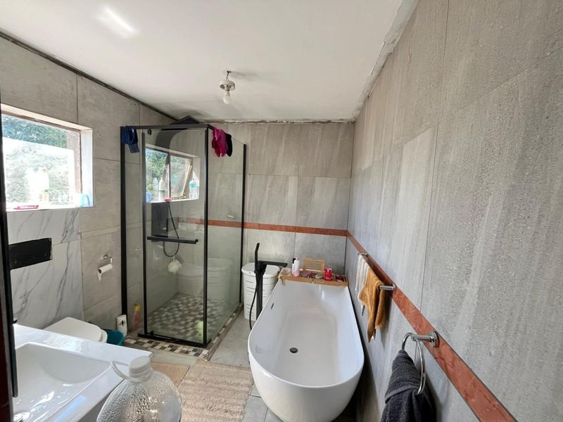 A bathroom featuring a freestanding bathtub, glass shower enclosure, wall-mounted toilet, and vanity basin with grey tiled walls and flooring.