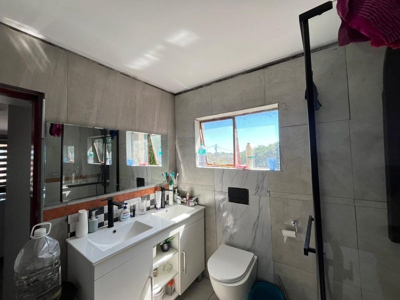Modern bathroom featuring a double vanity, wall-mounted toilet, and a walk-in shower with contemporary grey tiling.