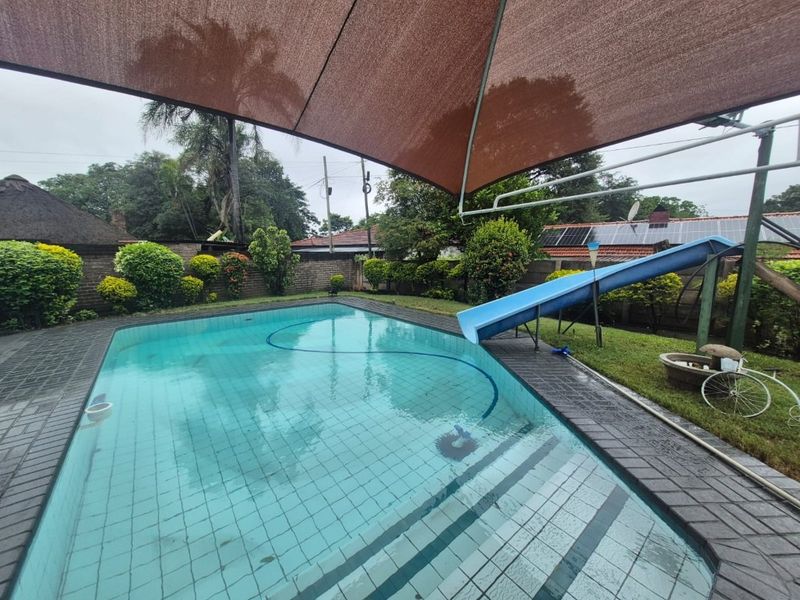 Outdoor pool area featuring a built-in slide, paved surround, and a large shade sail, set within a private garden with brick boundary walls.