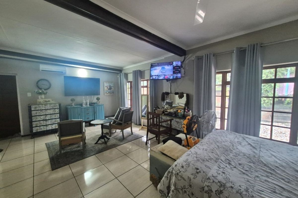 Spacious bedroom featuring tiled flooring, an exposed structural beam, ceiling fan, air conditioning, and direct access to the garden through glass-paned french doors.