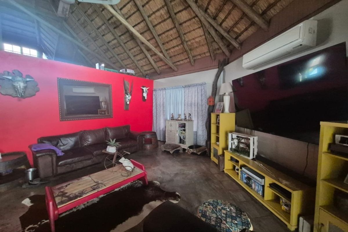 Spacious living room featuring a high vaulted thatched ceiling with exposed timber rafters, concrete flooring, and a wall-mounted air conditioning unit.