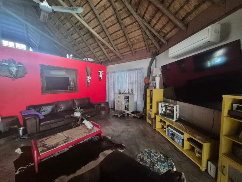 Spacious living room featuring a high vaulted thatched ceiling with exposed timber rafters, concrete flooring, and a wall-mounted air conditioning unit.
